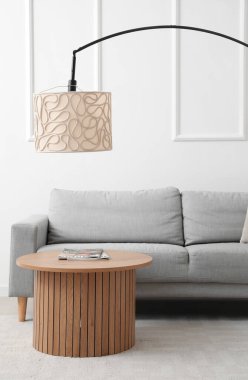 Sıcak gri kanepe, sehpa ve lamba beyaz duvarın yanında.