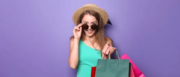 Schöne Junge Frau Mit Sonnenbrille Und Einkaufstaschen Auf Lila Hintergrund — Stockfoto