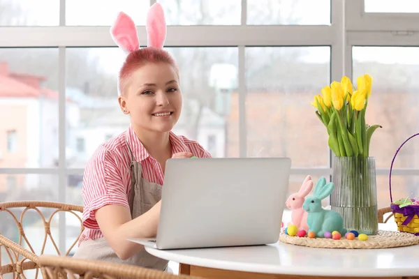 Paskalya Günü Mutfaktaki Masada Tavşan Kulaklı Laptoplu Genç Bir Kadın — Stok fotoğraf
