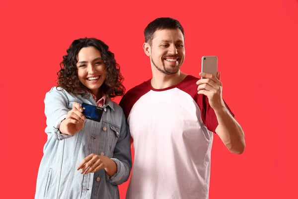 Young couple with credit card and mobile phone on red background