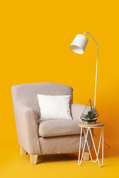 Cozy beige armchair, lamp and table with houseplant on orange background