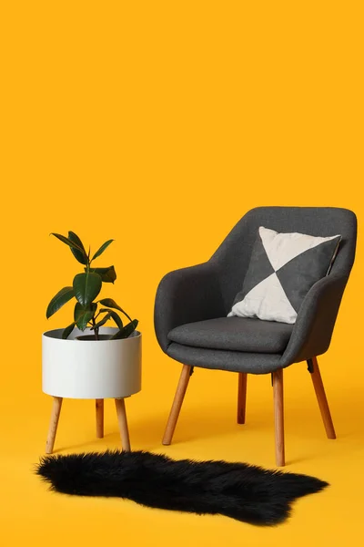 stock image Stylish grey armchair, houseplant in pot and fur rug on orange background