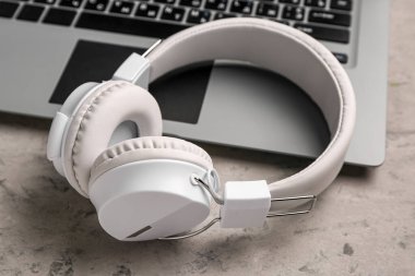 Gri grunge arka planda dizüstü bilgisayarı olan modern beyaz kulaklıklar.