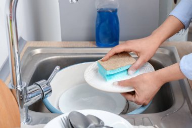 Bulaşıkları lavaboda süngerle yıkayan kadın.