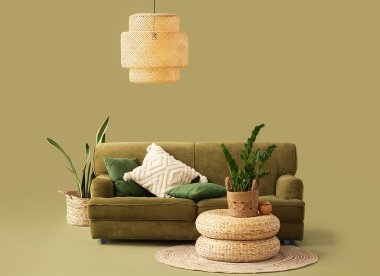 Sıcak kanepe, hasır puflar ve yeşil arka planda ev bitkileri.