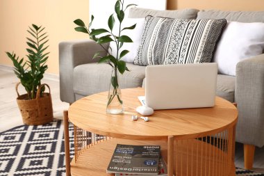 Modern dizüstü bilgisayarı, kulaklığı ve vazosu olan kahve masası oturma odasının içinde.