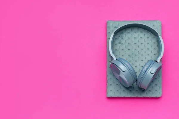 Modern blue headphones with notebook on pink background