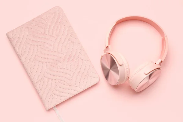 Modern headphones with notebook on pink background