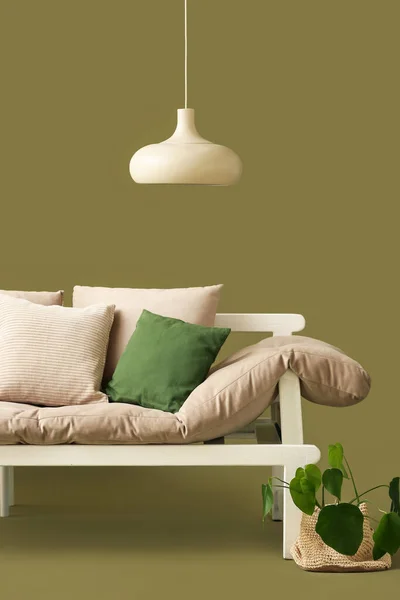 Cozy sofa with cushions, lamp and houseplant on green background