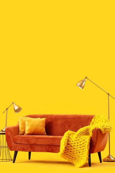 Stock image Cozy brown sofa with cushions and plaid on yellow background