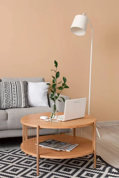 Coffee table with modern laptop, earphones and vase in interior of living room