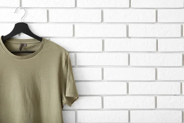 Stylish t-shirt hanging on white brick wall