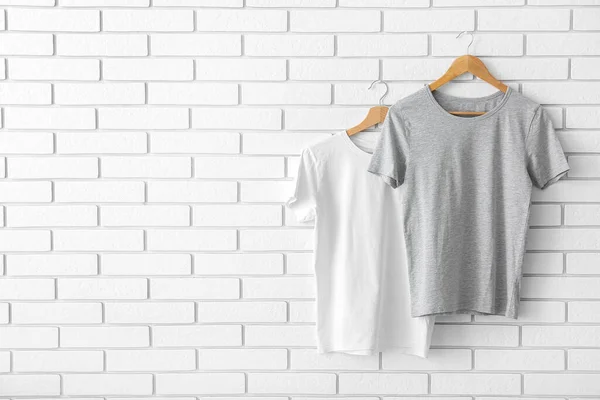 Stylish t-shirts hanging on white brick wall
