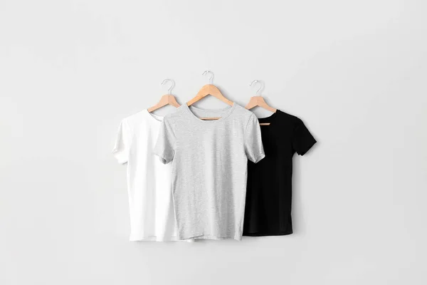 Stylish t-shirts hanging on grey wall