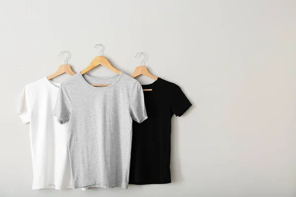 Stylish t-shirts hanging on grey wall
