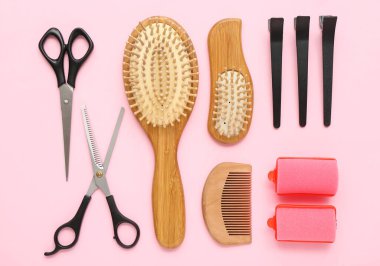 Pembe arka planda saç fırçaları, makas, ataç ve bigudiler.