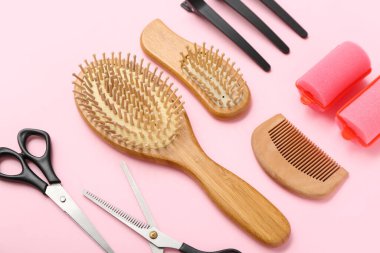 Pembe arka planda saç fırçaları, makas, ataç ve bigudiler, yakın plan.