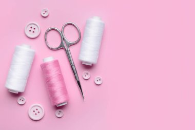 Pembe arka planda iplik makaralı, düğmeli ve makaslı kompozisyon