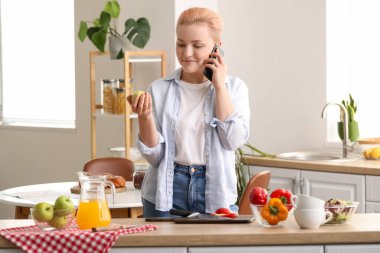 Elmalı genç bir kadın mutfakta cep telefonuyla konuşuyor.