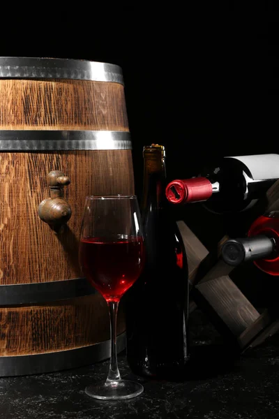 Oak barrel with bottles and glass of wine on dark background