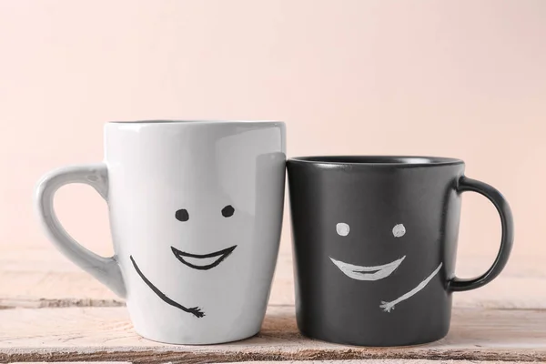 Cups with happy faces on white wooden table. Friendship Day celebration