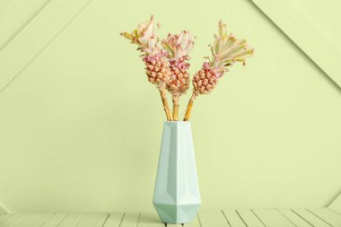 Yeşil duvarın yanındaki masada süs anananaslı vazo.