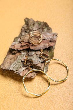 Altın küpeli ağaç kabuğu ve bej arka planda yüzük, yakın plan.