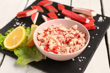 Bowl with tasty chopped crab sticks on light wooden background clipart