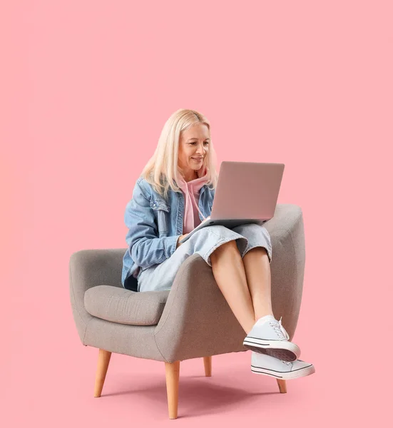 Volwassen Vrouwelijke Programmeur Werken Met Laptop Fauteuil Roze Achtergrond — Stockfoto
