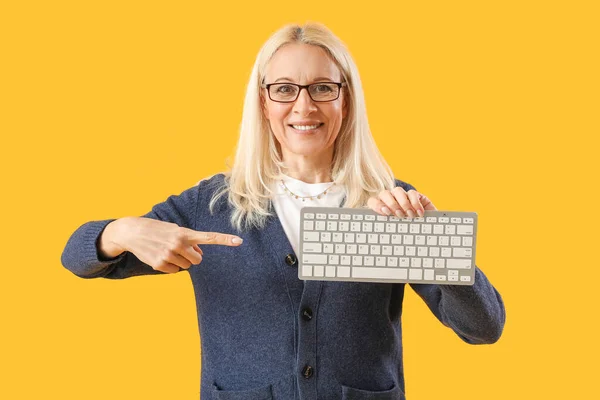 Mature female programmer pointing at computer keyboard on yellow background