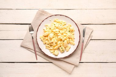 Çırpılmış yumurta tabağı ve beyaz ahşap arka planda çatal bıçak.