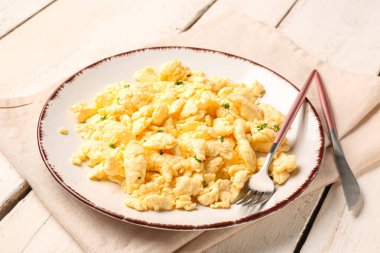 Çırpılmış yumurta tabağı ve beyaz ahşap arka planda çatal bıçak.