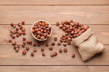 Tahta arka planda kabuklu fındık kabuğu olan çuval ve kase.