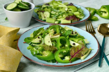 Yeşil sebzeli salata tabakları ve ahşap arka planda malzemeler.