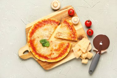 Parmesan peynirli ahşap tahta pizza, fesleğen ve gri arka planda kesici.