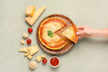 Gri arka planda parmesan peynirli lezzetli bir pizza alan bir kadın.