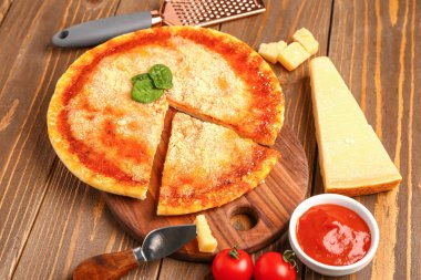 Tahta arka planda parmesan peynirli, fesleğenli ve rendelenmiş lezzetli pizza.