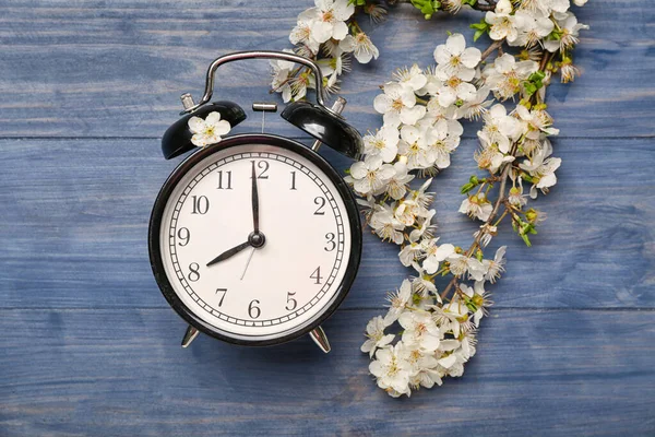 春の枝や青木製の背景に黒い目覚まし時計を開花 — ストック写真