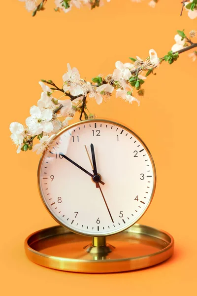 Blooming spring branches and golden clock on orange background
