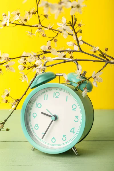 Virágzó Tavaszi Ágak Kék Ébresztőóra Zöld Asztalon Sárga Fal Közelében — Stock Fotó