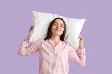 Young woman with soft pillow on lilac background