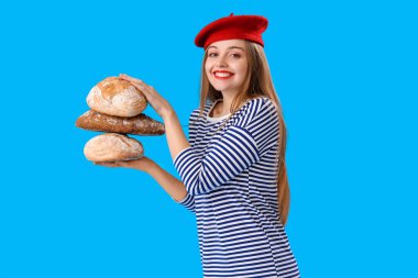 Young woman in beret with loaves of fresh bread on blue background