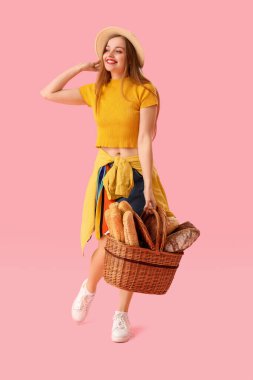 Young woman in hat with basket of fresh bread on pink background