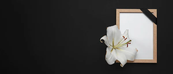 Photo frame with black funeral ribbon and lily flower on dark background with space for text