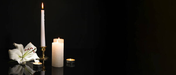 Burning candles and lily flower on dark background with space for text. Funeral concept