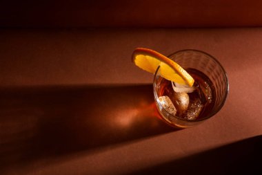 Bir bardak buzlu rom ve kahverengi arka planda portakal dilimi.