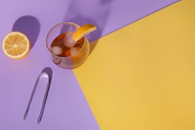 Bir bardak buzlu rom, limon dilimi ve renkli arka planda maşa.