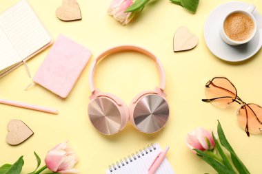 Modern kulaklıklar, not defterleri, güneş gözlükleri, bir fincan kahve ve renkli lale çiçekleri ile kompozisyon