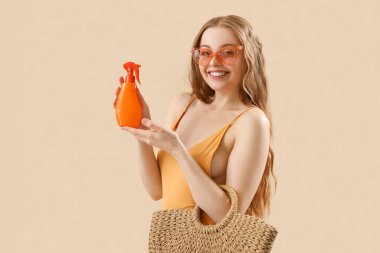 Bej arka planda güneş kremi ve plaj çantası olan güzel genç bir kadın.