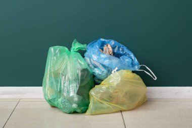 Yeşil duvarın yanında çöp torbaları var.